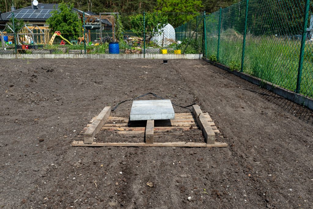 Leveling the chernozem in the yard with a pallet weighted with a concrete cube, preparing for lawn.